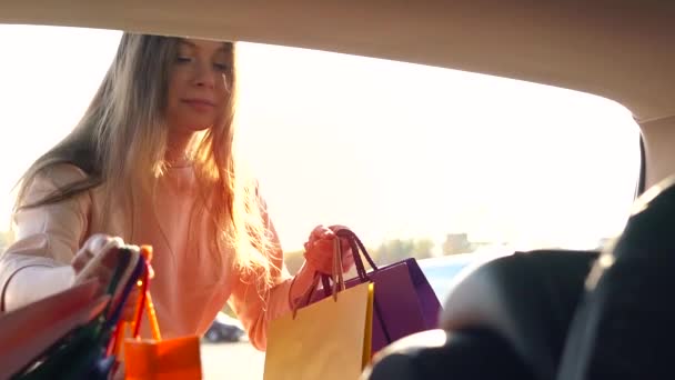 Beautiful girl puts shopping bags in the trunk of a car and leaves, intending to drive away. Slow motion. - Video