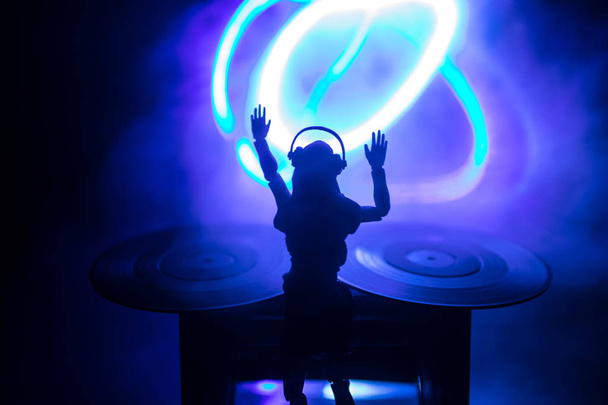 Dj club concept. Woman DJ mixing, and Scratching in a Night Club. Girl silhouette on dj's deck, strobe lights and fog on background. Creative artwork decoration with toy. Selective focus - Zdjęcie, obraz