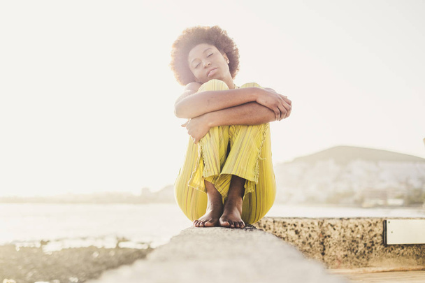 Афро-американская прическа девушка сидит и обнимает себя на открытом воздухе
  - Фото, изображение
