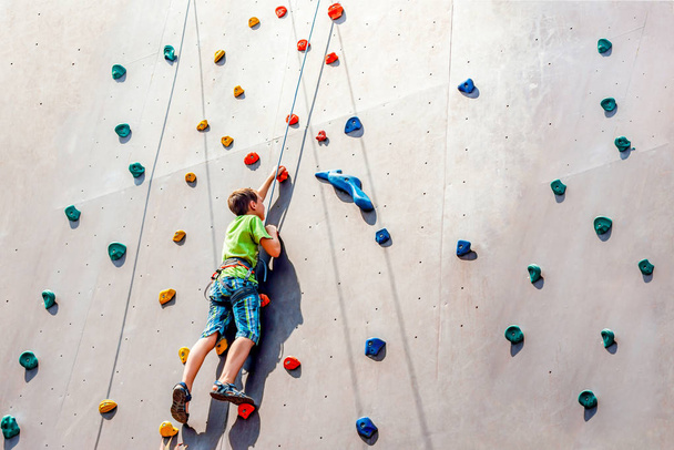 El niño escalador sube a una torre artificial, superando obstáculos en su camino hacia arriba
. - Foto, Imagen