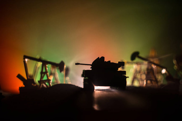 Resim dekorasyon. Petrol savaş kavramı. Askeri siluetleri, pompalar ve kulelerimiz petrol sahası. Puslu renkli gökyüzü arka plan. Zırhlı araçlar mücadele sahne. Seçici odak - Fotoğraf, Görsel