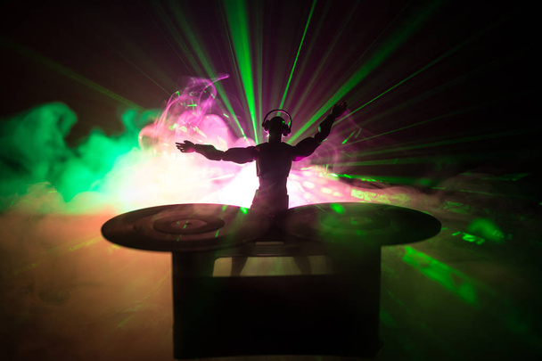 Dj club concept. DJ mixing, and Scratching in a Night Club. Man silhouette on vinyl turntable, strobe lights and fog on background. Creative artwork decoration with toy. Selective focus - Photo, Image