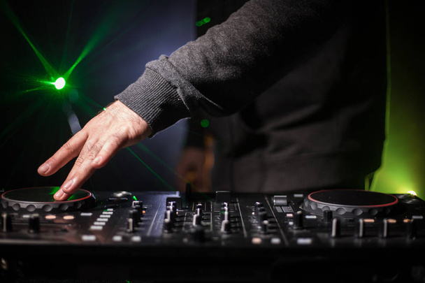 DJ spinnen, mixen en scratchen in een nachtclub, handen van dj tweaken verschillende track besturingselementen op dj's dek, strobe lights en mist, of Dj mixt de track in de discotheek op feestje. Selectieve aandacht - Foto, afbeelding