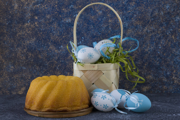 Easter bread and blue Easter eggs in a basket on dark stone table - Photo, Image