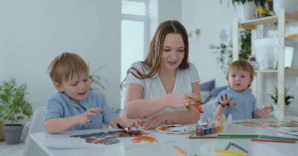 De familie heeft leuke schilderij op papier met hun vingers in paint. Moeder en twee kinderen schilderen met vingers op papier - Video