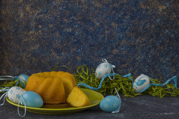 Pan de Pascua en plato verde y huevos de Pascua pintados en mesa de piedra oscura decorada con hierba verde
 - Foto, imagen