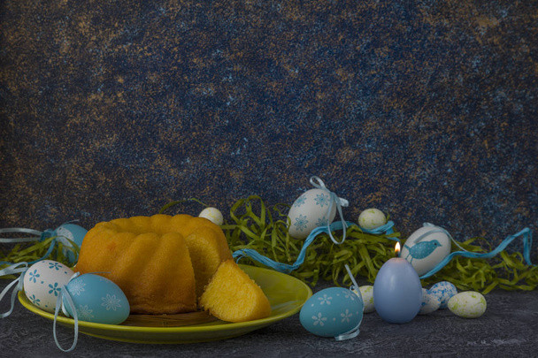 Pão de Páscoa na placa verde e ovos de Páscoa pintados na mesa de pedra escura decorada com grama verde
 - Foto, Imagem