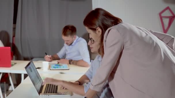 Žena se blíží k dělníkovi v kanceláři a prohlíží si tabulky v laptopu - Záběry, video