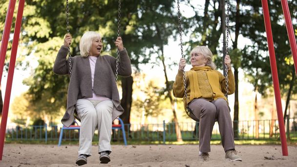 Two senior ladies enjoying ride on swings in park, elderly friends, retirement - Foto, afbeelding