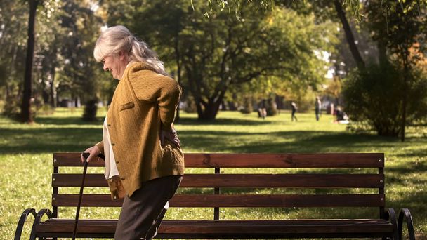 Senior lady slowly walking with stick along park suffering from back pain - Φωτογραφία, εικόνα