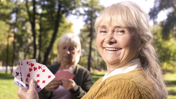 Allegra vecchia che mostra carte da gioco e sorridente seduta nel parco, relax
 - Foto, immagini