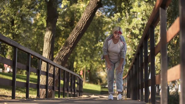 Sportive starszy pani trzyma jej kolana uczucie ostry ból podczas joggingu, zdrowie - Zdjęcie, obraz