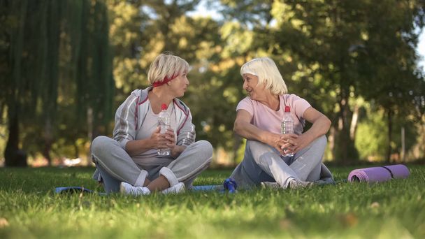 Женщина средних лет и ее мать разговаривают после занятий спортом и йогой в парке
 - Фото, изображение