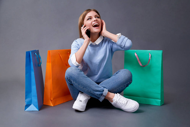 Young woman talking on your smartphone sitting with colored bags for shopping. - Fotografie, Obrázek