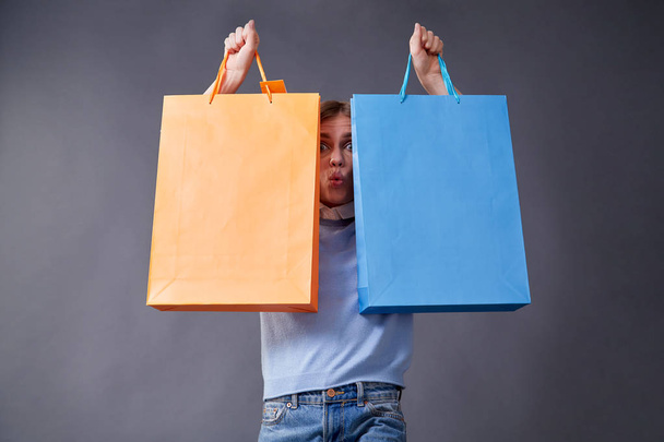 Emotional girl with colored bags standing on a gray background. - Foto, immagini