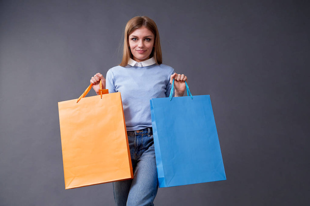 Emotional girl with colored bags standing on a gray background. - Foto, imagen