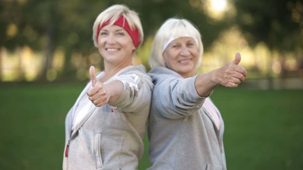 Two happy mature women smiling and showing thumbs up in park, healthy lifestyle - Foto, Imagen