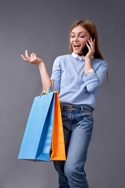 Young woman talking on your smartphone standing with colored bags for shopping. - Foto, imagen