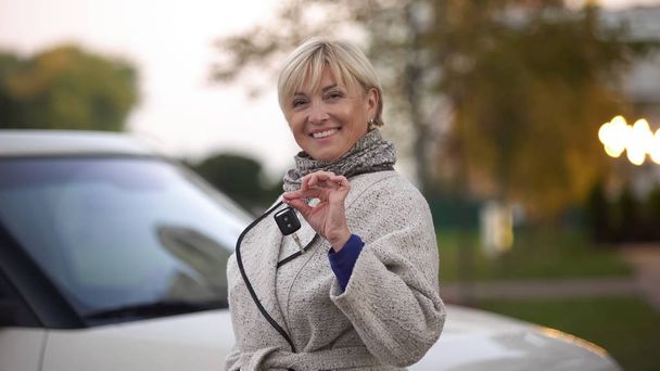 Mature successful woman smiling and holding keys of new luxury car, present - Фото, изображение