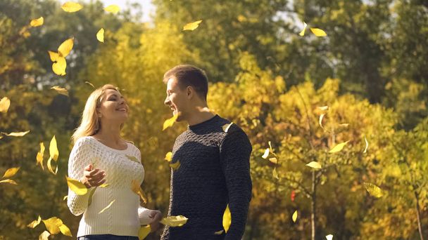 Carefree couple enjoying yellow leaves falling down, happy childish moments - 写真・画像