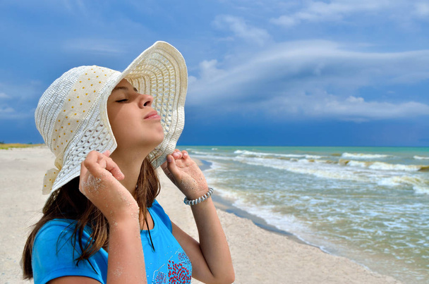 Genç kız deniz sahilde beyaz şapkalı. Mavi deniz karşı temiz, kumlu plaj. - Fotoğraf, Görsel