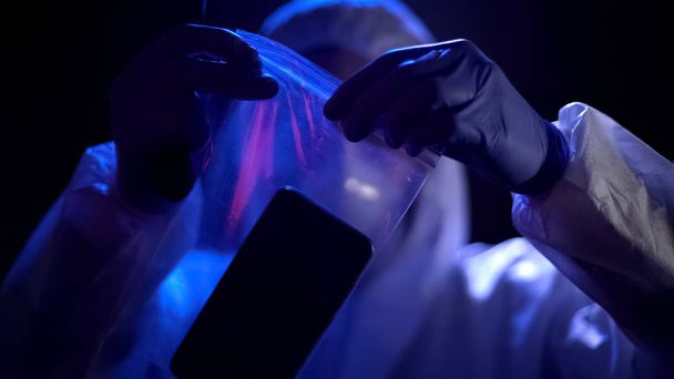 Criminal expert putting smartphone with criminal fingerprints in plastic bag - Foto, imagen