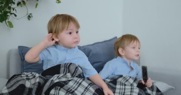 4 と 2 歳の 2 人の少年は、ソファに座ってテレビを見ています。エキサイティングなテレビ番組。漫画を表示します。子供たちは、刺激的なテレビ番組を見る. - 映像、動画