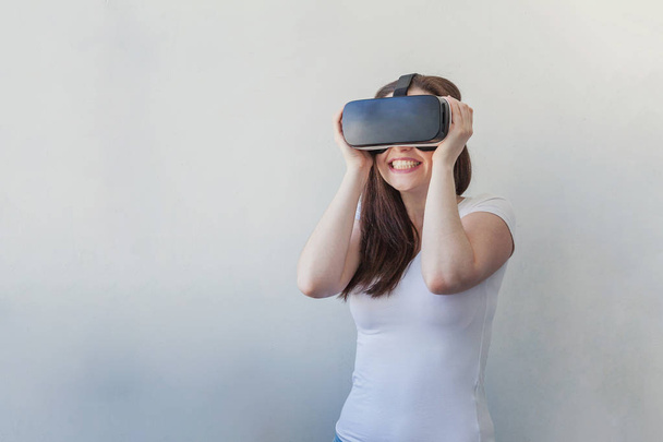 Hymyile nuori nainen yllään käyttäen virtuaalitodellisuus VR lasit kypärä kuulokkeet valkoisella taustalla
 - Valokuva, kuva