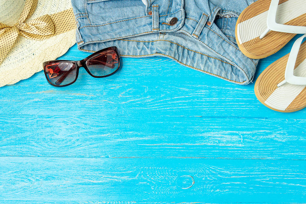 Frame elegant female straw hat slippers jeans sunglasses on blue wooden background, copyspace for text, summer vacation. - Фото, зображення