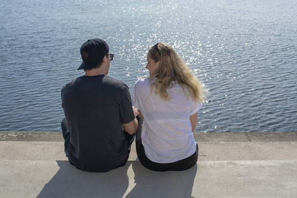 junges Paar sitzt in der Sonne und schaut zu, wie Wasser auf Steinmole glitzert  - Foto, Bild