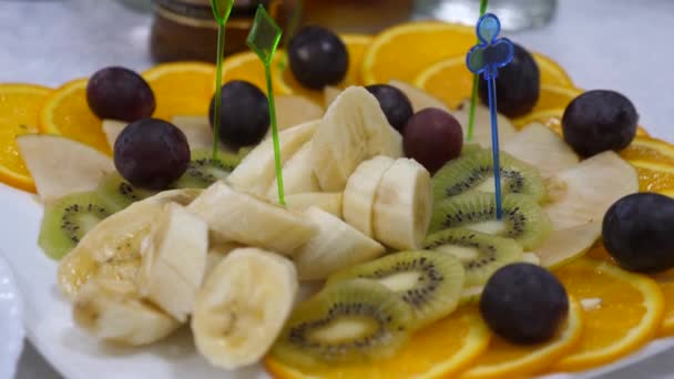 Banaj, pomeranče, hrozny, kiwi plátky, detail. Čerstvé ovoce jídlo na slavnostní jídelní stůl. Špejle různé plátky ovoce na talíři. - Záběry, video