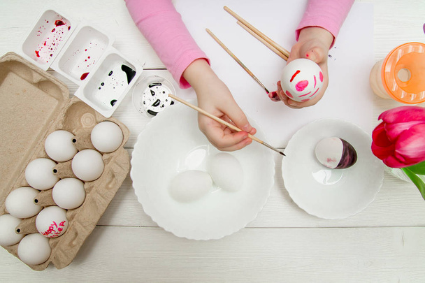 A flat lay with kids hands painting Easter eggs on white wooden table - Foto, Imagem