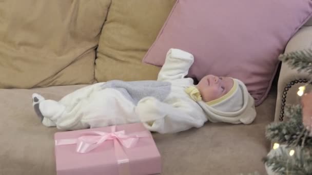 Ένα νεογέννητο είναι ξαπλωμένο στον καναπέ κοντά στο χριστουγεννιάτικο δέντρο.. - Πλάνα, βίντεο