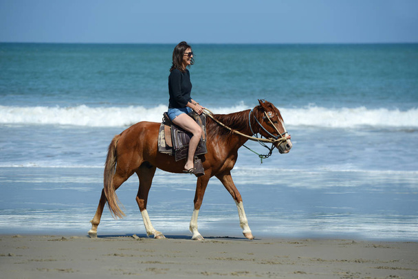 Mulher montando em um cavalo ao longo da costa do oceano
 - Foto, Imagem