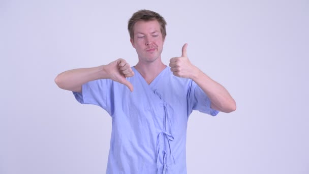 Confused young man patient choosing between thumbs up and thumbs down - Filmagem, Vídeo