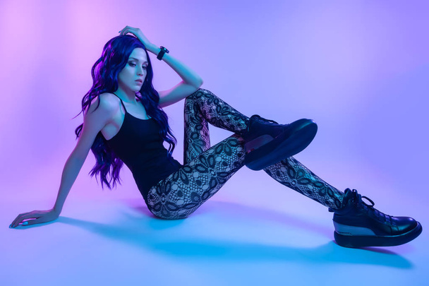 Beautiful woman with long purple hair in black underwear, pantyhose posing in attractive position in colorful bright neon blue and pink lights in studio. Fashion concept - Fotó, kép