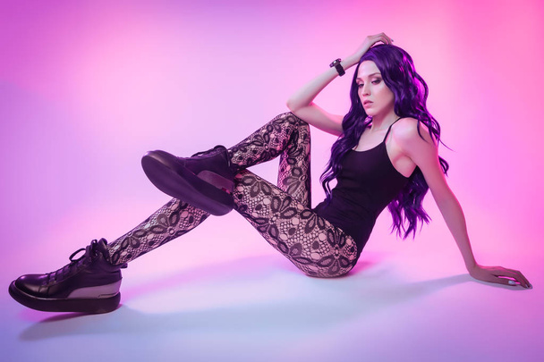 Belle femme avec de longs cheveux violets en sous-vêtements noirs, collants posant dans une position attrayante dans des lumières lumineuses colorées bleu néon et rose en studio. Concept de mode
 - Photo, image