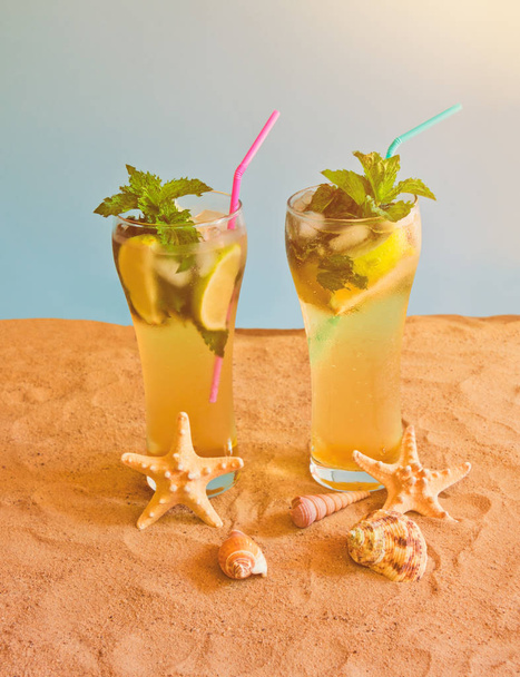 Two glasses of mojito cocktail with drinking straws on sand beach on blue backdrop.  - 写真・画像