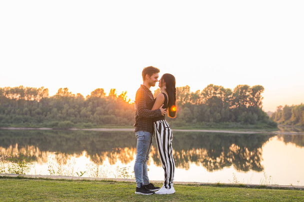 Ρομαντική και άνθρωποι έννοια - νεαρό ζευγάρι αγκάλιασμα μαζί κοντά στο ποτάμι ή λίμνη και απολαμβάνοντας την θερινή ώρα - Φωτογραφία, εικόνα