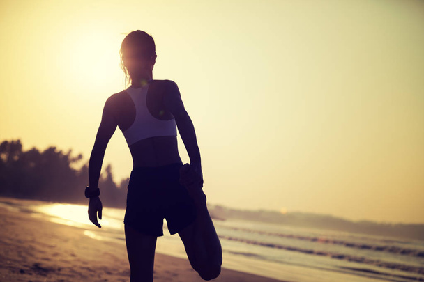 sportswoman warming up on sunrise beach - 写真・画像