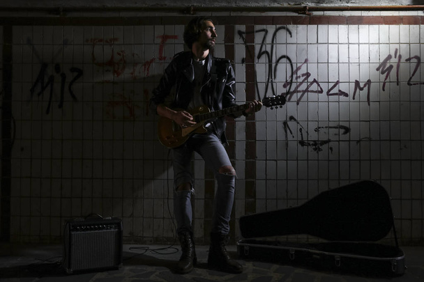 Un músico callejero tocando la guitarra en el paso subterráneo. Un estilo de vida vagabundo. Jugando en el paso subterráneo para ganarse la vida. Músico desempleado. Futura estrella del rock
. - Foto, imagen