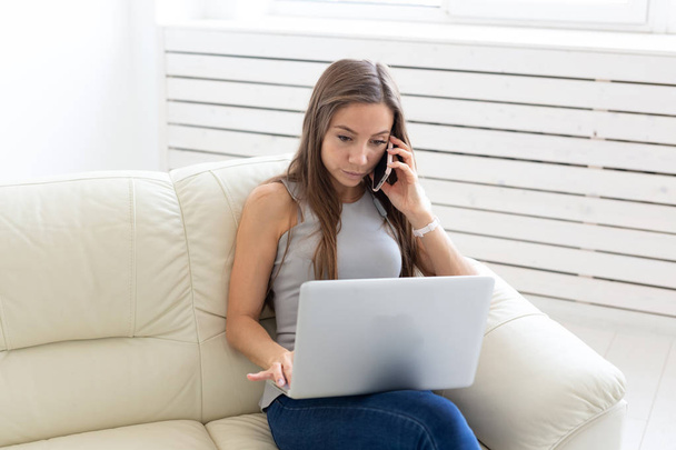 Business, freelance ja ihmiset käsite - Nuori nainen istuu sohvalla ja puhuu puhelimessa
 - Valokuva, kuva