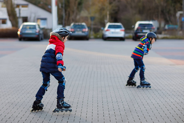 Két kisfiú görkorcsolyázik a városban. Boldog gyerekek, testvérek és legjobb barátok védőruhában. Aktív iskolások, akik sportolnak és megtanulnak korcsolyázni az inline korcsolyázókon. - Fotó, kép