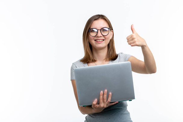 Ανθρώπους και εκπαίδευση έννοια - ελκυστικό φοιτητής γυναίκα κρατώντας ένα φορητό υπολογιστή και να δείχνει τον αντίχειρα επάνω σε λευκό φόντο - Φωτογραφία, εικόνα