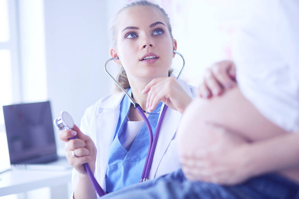 Jonge vrouwelijke arts onderzoekt zwangere vrouw in de kliniek. - Foto, afbeelding