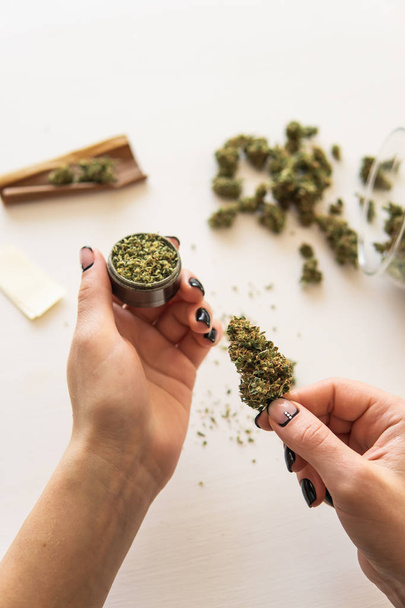 Close up of marijuana blunt with grinder. marijuana use concept. Woman rolling a cannabis blunt on white background. Woman preparing and rolling marijuana cannabis joint. - Photo, Image