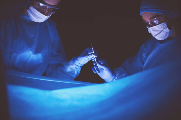 Doctors team in surgery in a dark background. - Zdjęcie, obraz