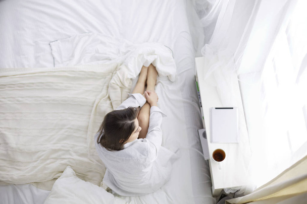 Portrait de femme utilisant un comprimé et buvant du café assis sur le lit le matin - Photo, image