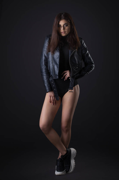 Brunette girl in a black leather jacket . Beautiful model on a dark background. - Photo, image
