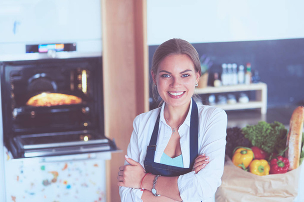 Portrait of young woman standing with arms crossed against kitchen background - Foto, Bild